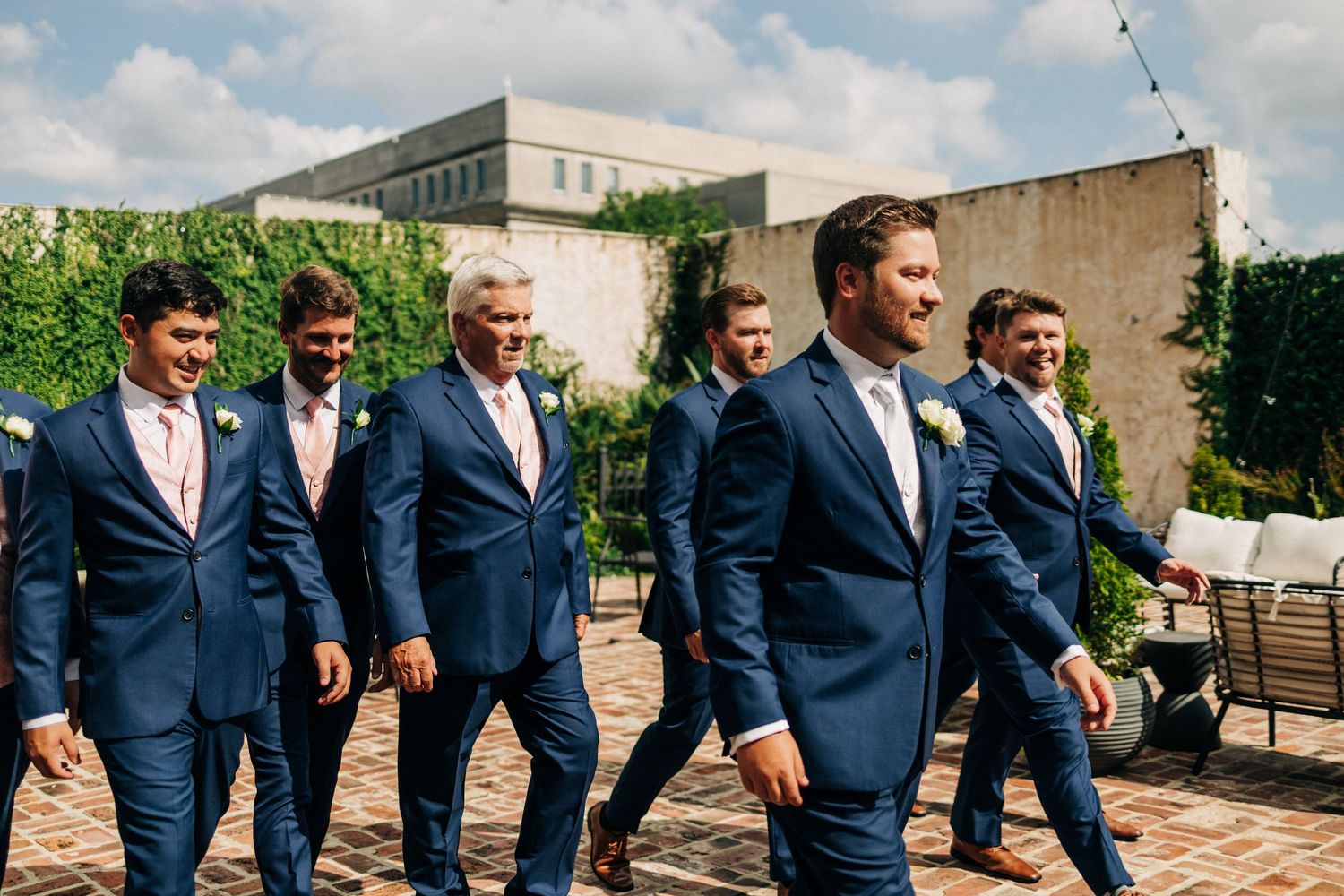 Groomsmen in matching navy blue suits share laughter and candid moments during outdoor wedding photography session.