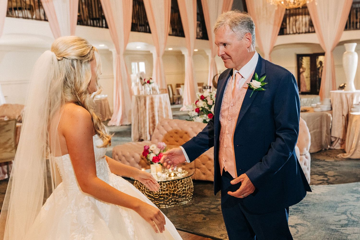 Two people share a joyful moment while dancing in an elegant ballroom with white columns and drapes.