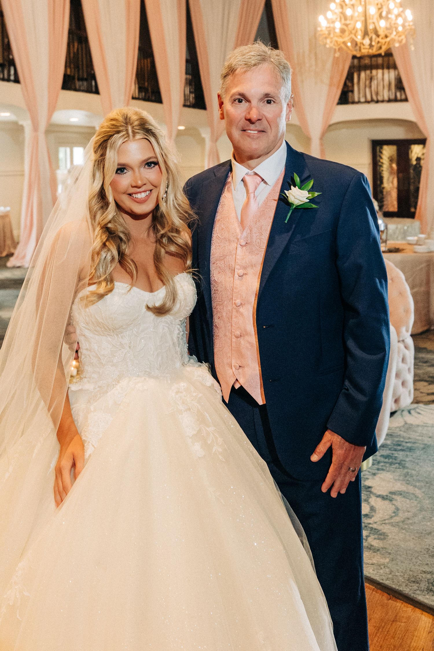A couple poses together at their wedding reception with elegant draping and chandeliers in the background.