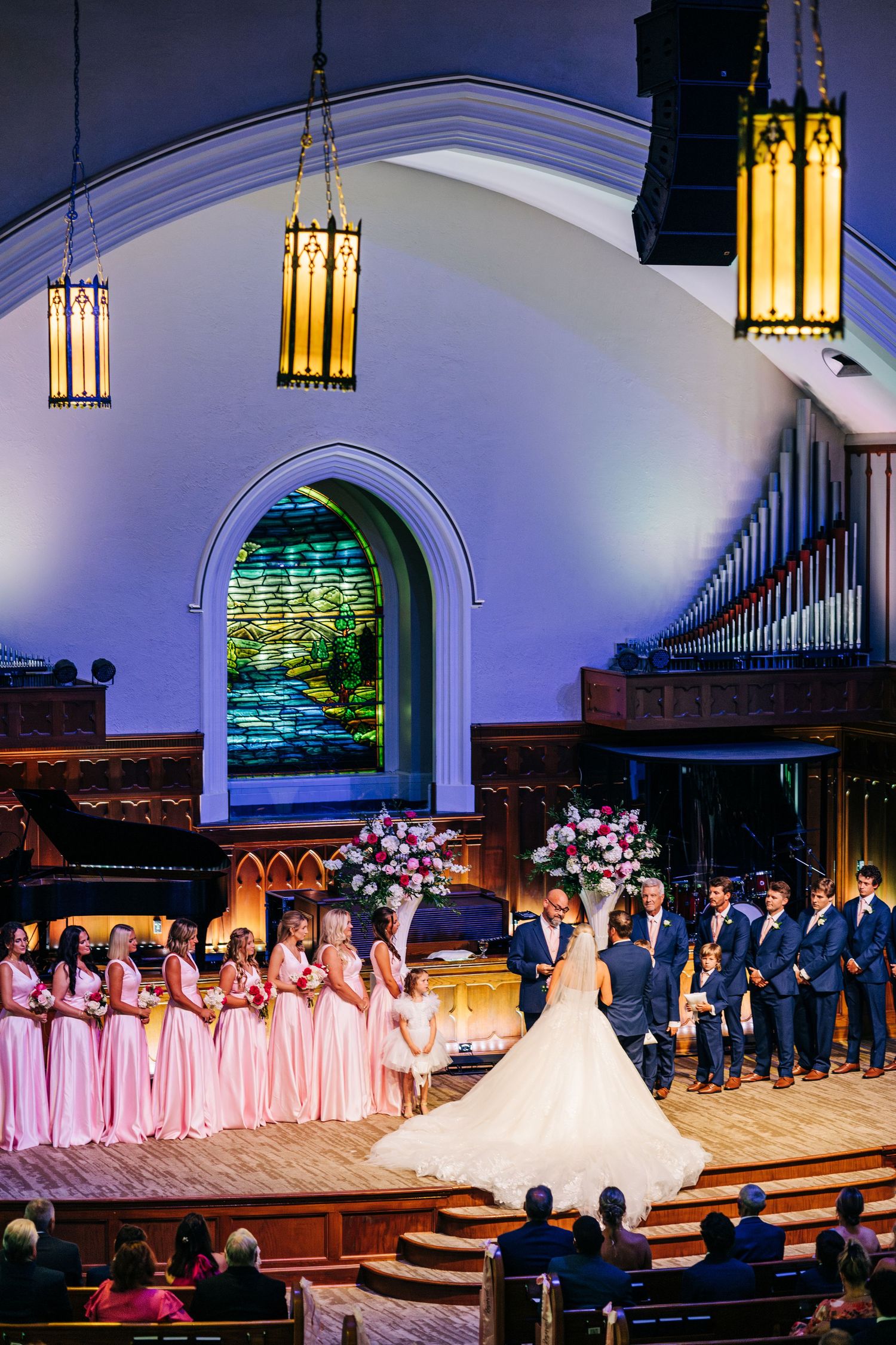 Wedding ceremony setup in an elegant church with bridesmaids in pink dresses and groomsmen lined up at the altar.