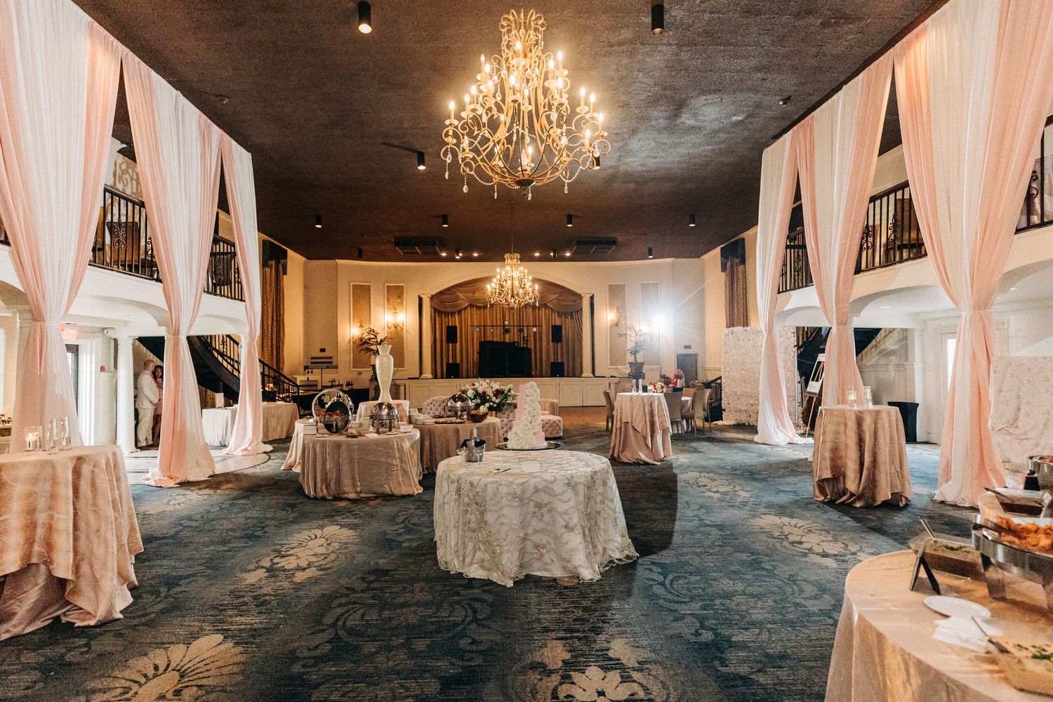 Elegant wedding reception venue with crystal chandelier, draped white fabric, and vintage-style decor in muted tones.