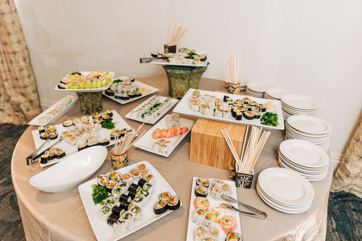 Various plates of sushi rolls and appetizers arranged on a round table with white plates and wood serving boards.