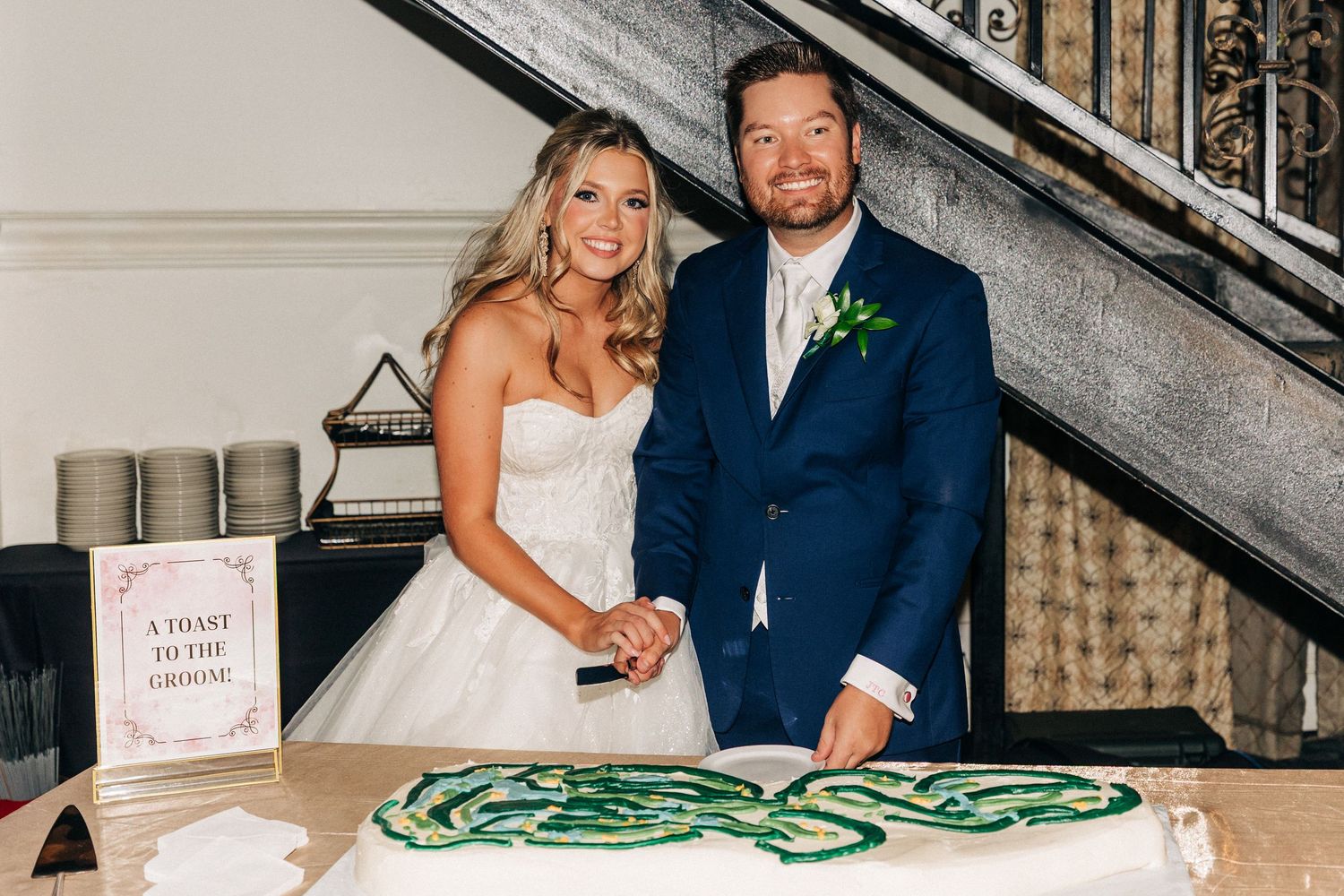 A couple stands together at their wedding reception next to a table with green snake decorations.