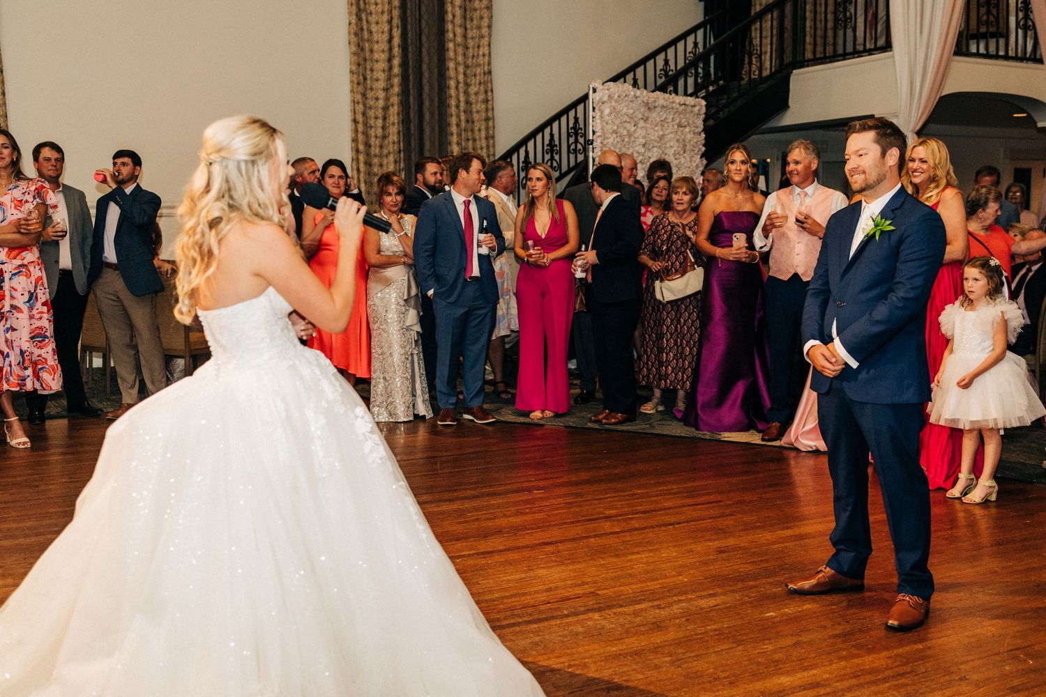 People dancing during a wedding reception in elegant formal attire at a grand ballroom venue.