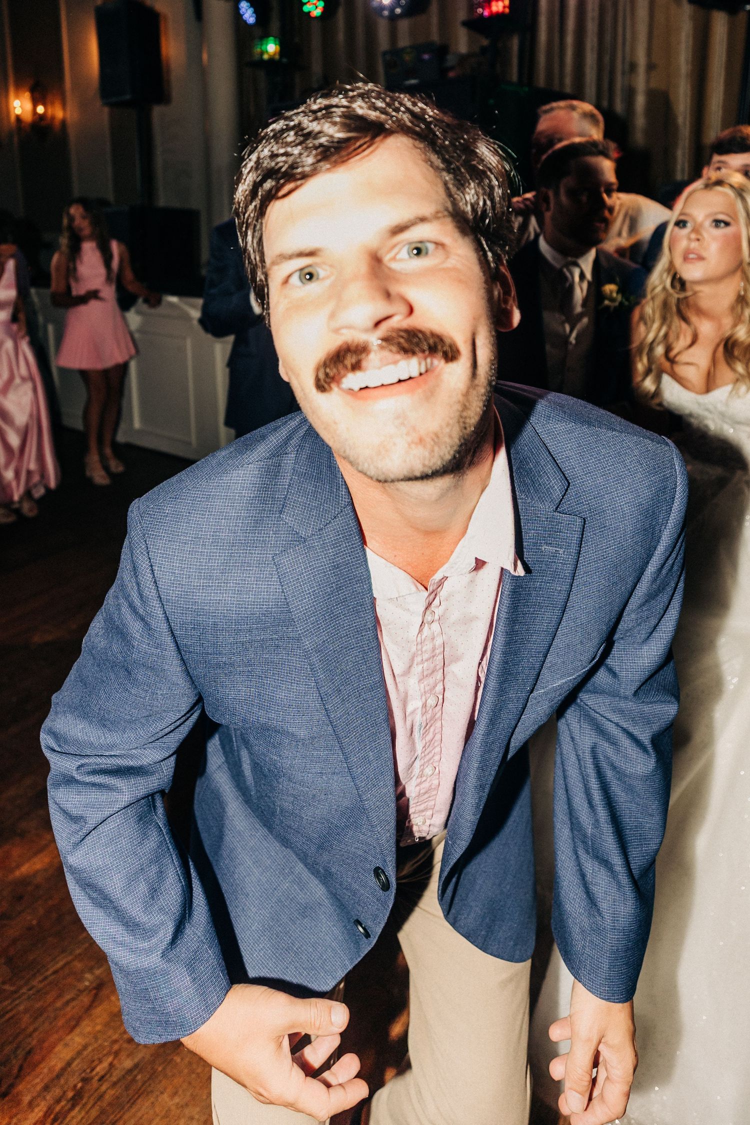 A sequence of four candid party photos showing someone in a blue blazer and pink shirt smiling at the camera on a wooden floor.