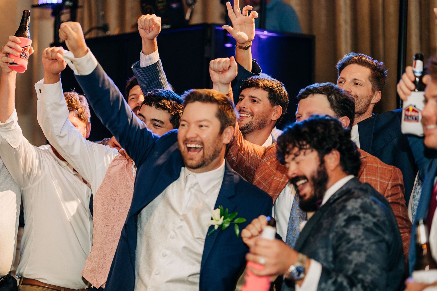 Group of excited partygoers celebrating with drinks at an event, cheering and raising their hands in joy.