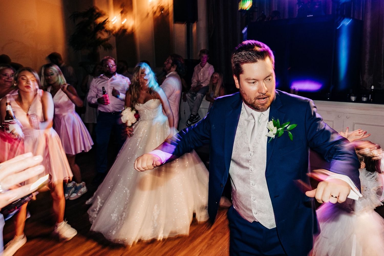 Couples dance together at an elegant wedding reception with colorful mood lighting and festive atmosphere.