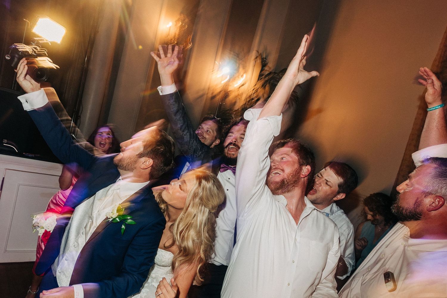 Party guests dance enthusiastically with raised hands and excited expressions during a lively indoor celebration.