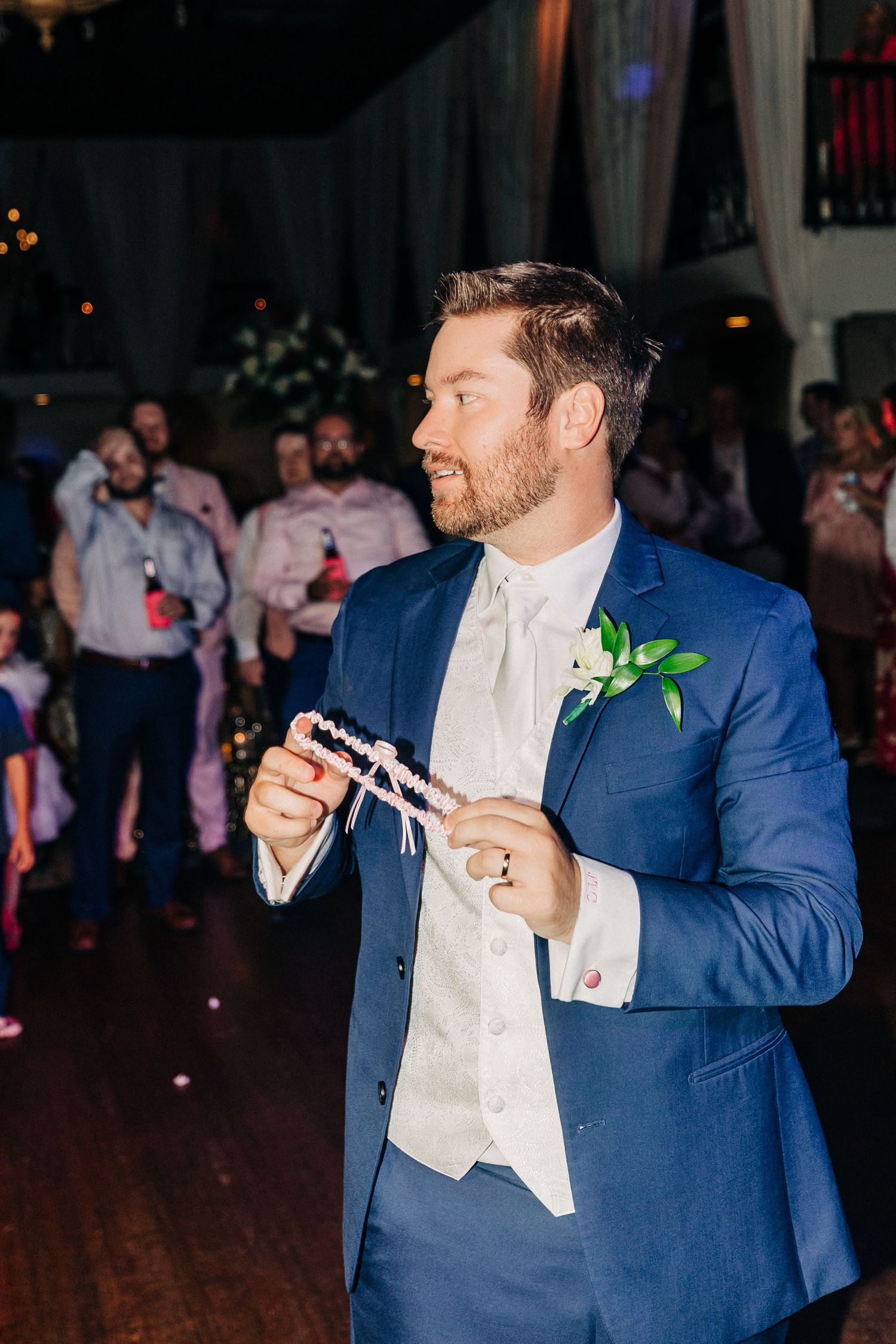 A person in a blue suit and white vest holds a sparkler while dancing at a wedding reception.