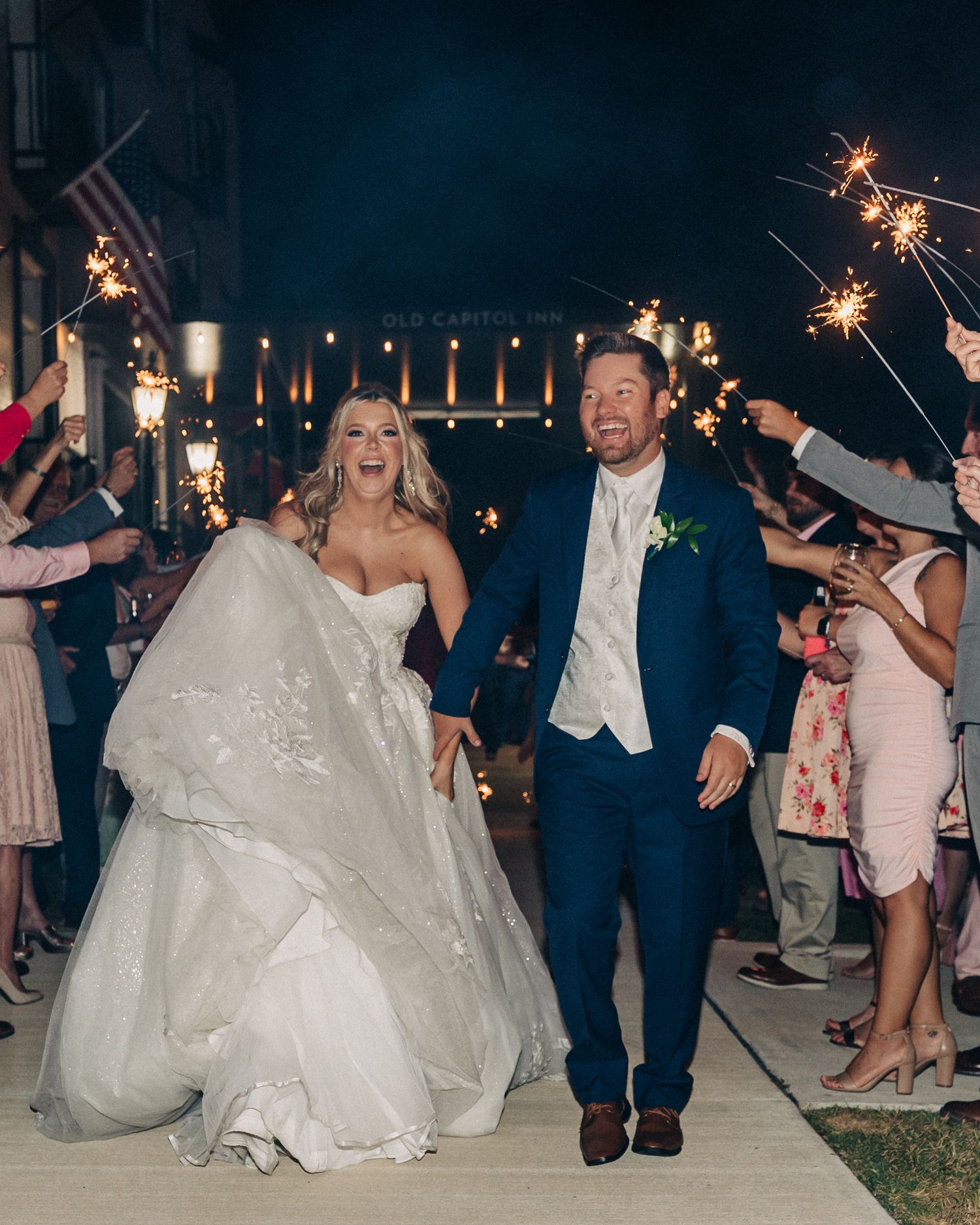 Happy newlyweds make their sparkler exit from their wedding celebration, surrounded by guests and twinkling lights.