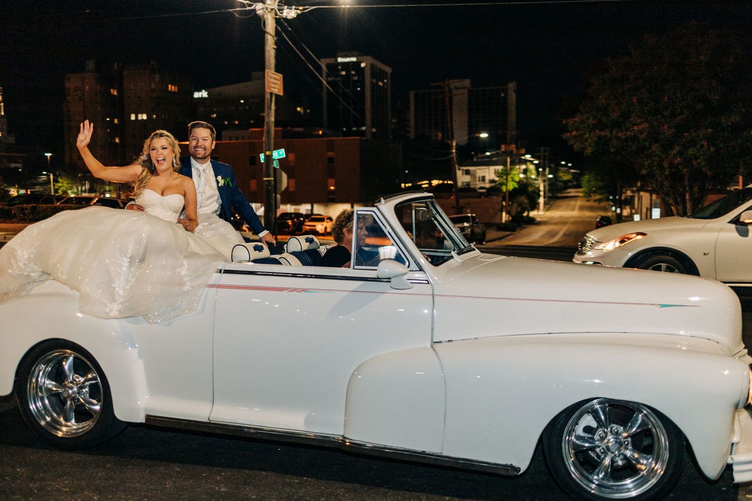 A classic white convertible car parked at nighttime during what appears to be a wedding celebration.