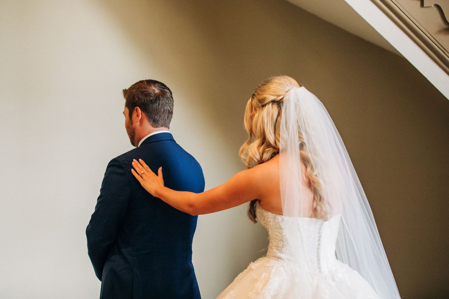 Bride in white wedding dress touches the shoulder of her partner before a first look moment at their wedding ceremony.