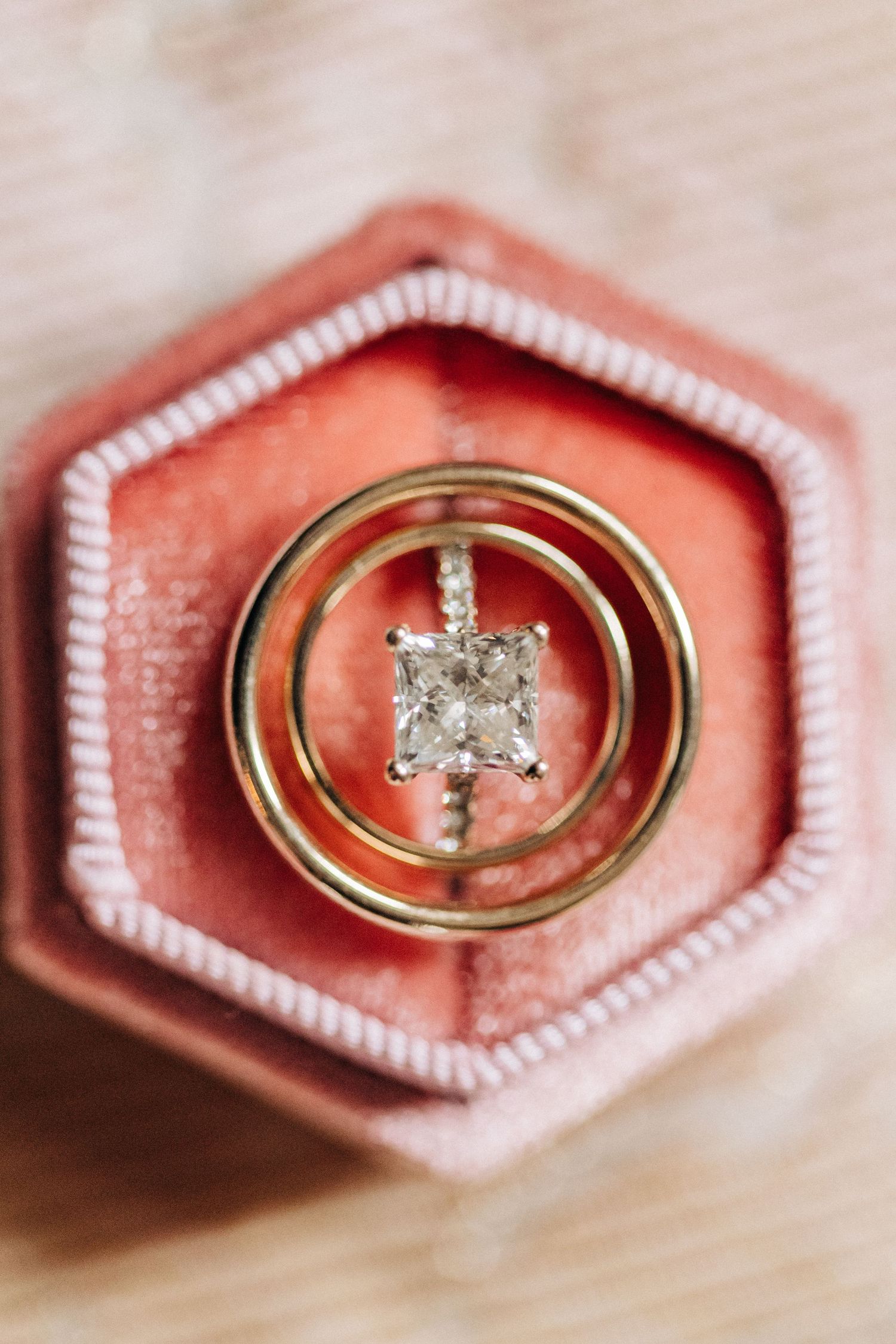 A diamond engagement ring and wedding band rest in a coral pink hexagonal ring box with white trim.
