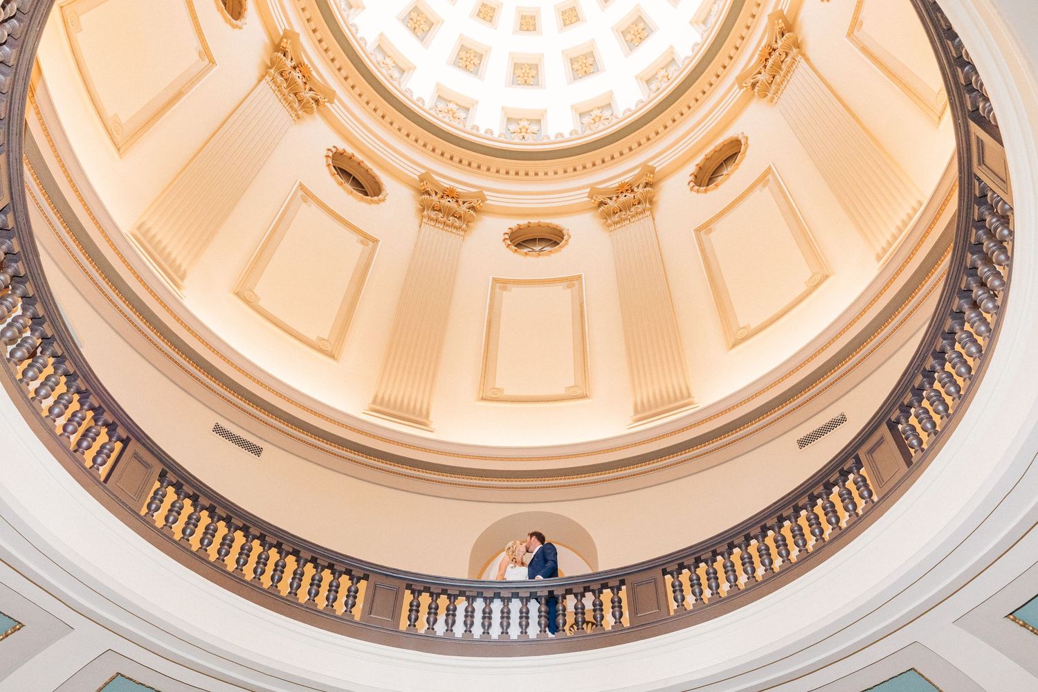 A grand circular rotunda with ornate architectural details and a domed ceiling featuring decorative moldings and railings.