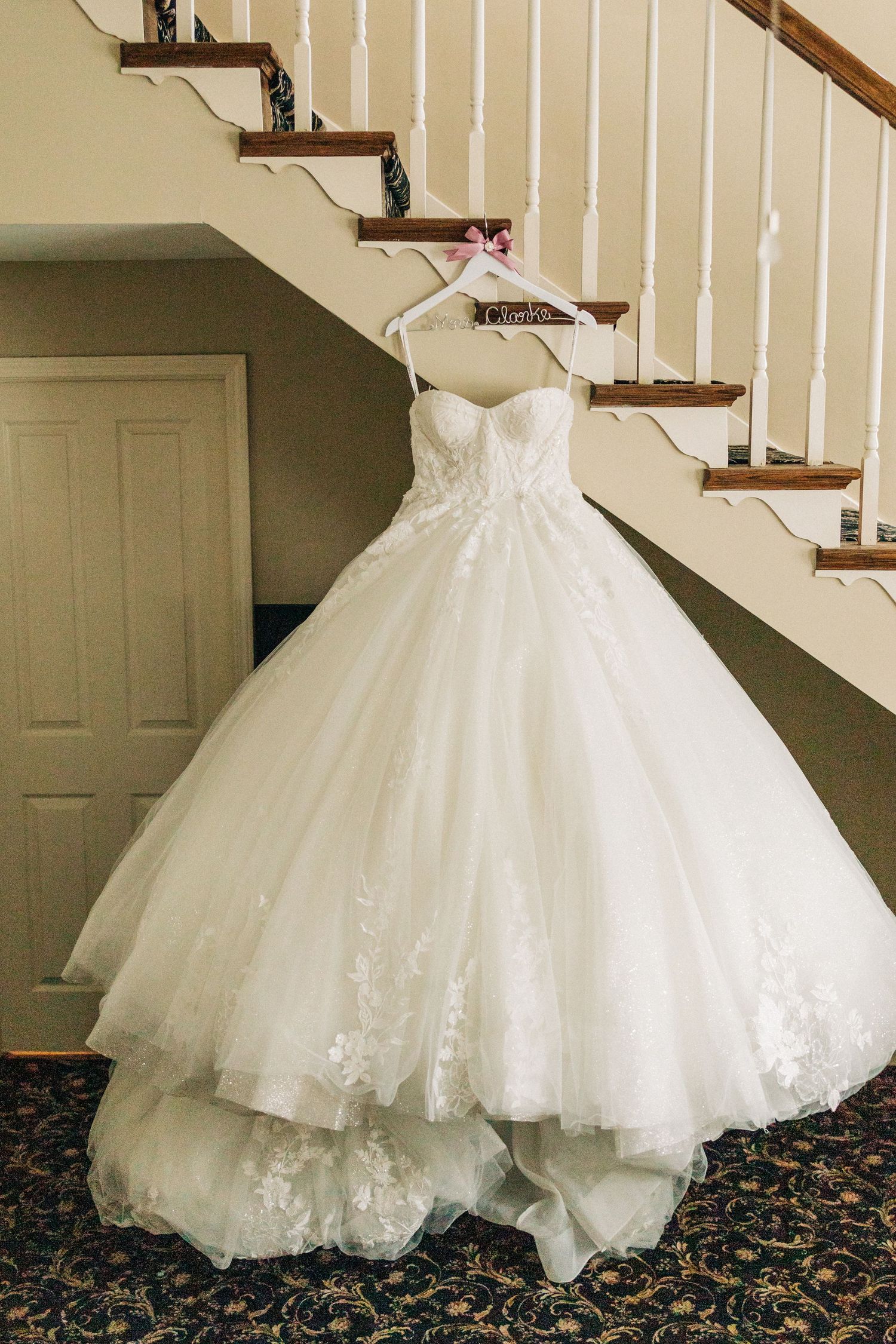 A stunning white wedding dress with tulle skirt and lace details displayed elegantly against a carpeted staircase.
