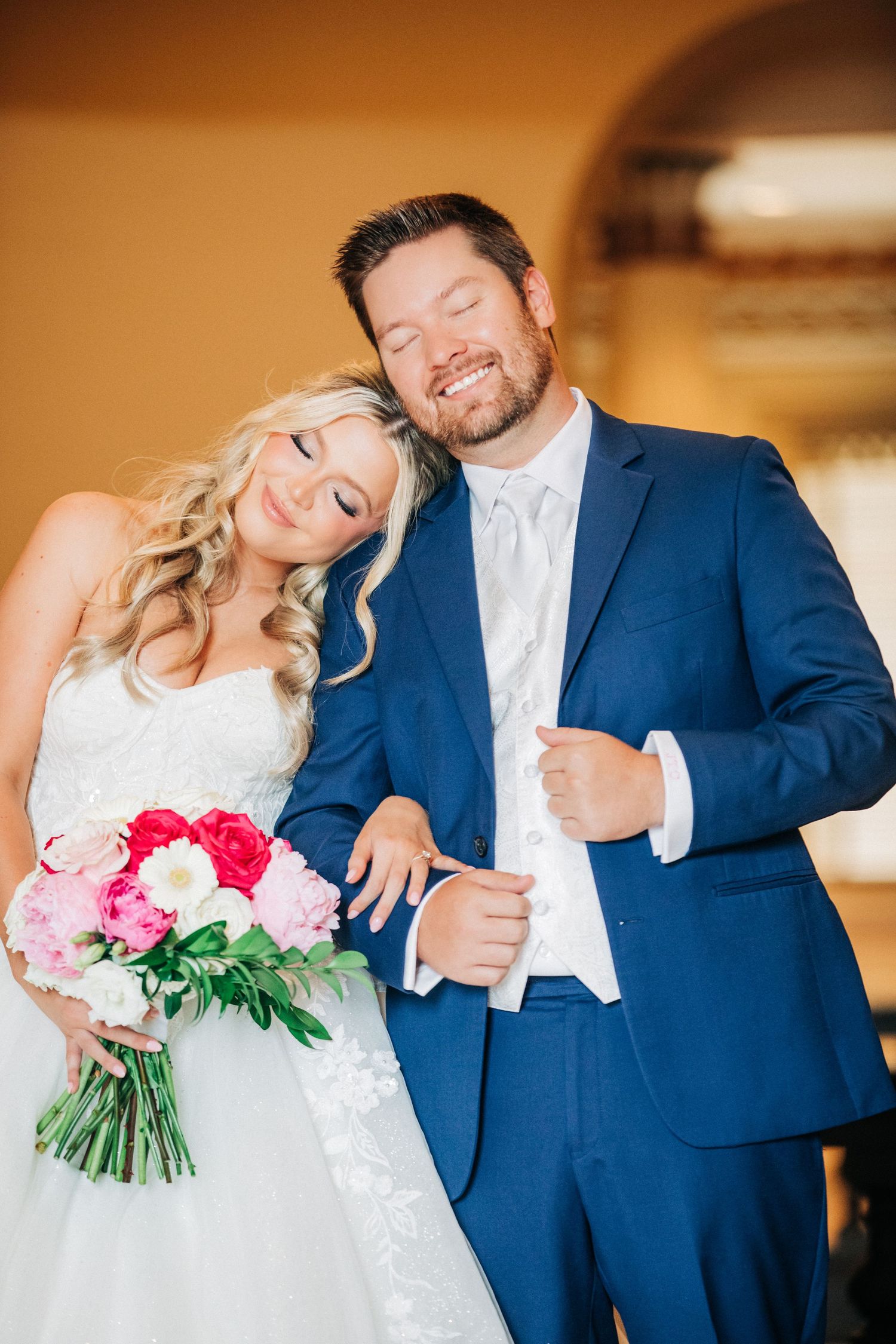 Newlyweds share candid laughing moments in a series of photos wearing navy suit and white wedding dress with pink bouquet.