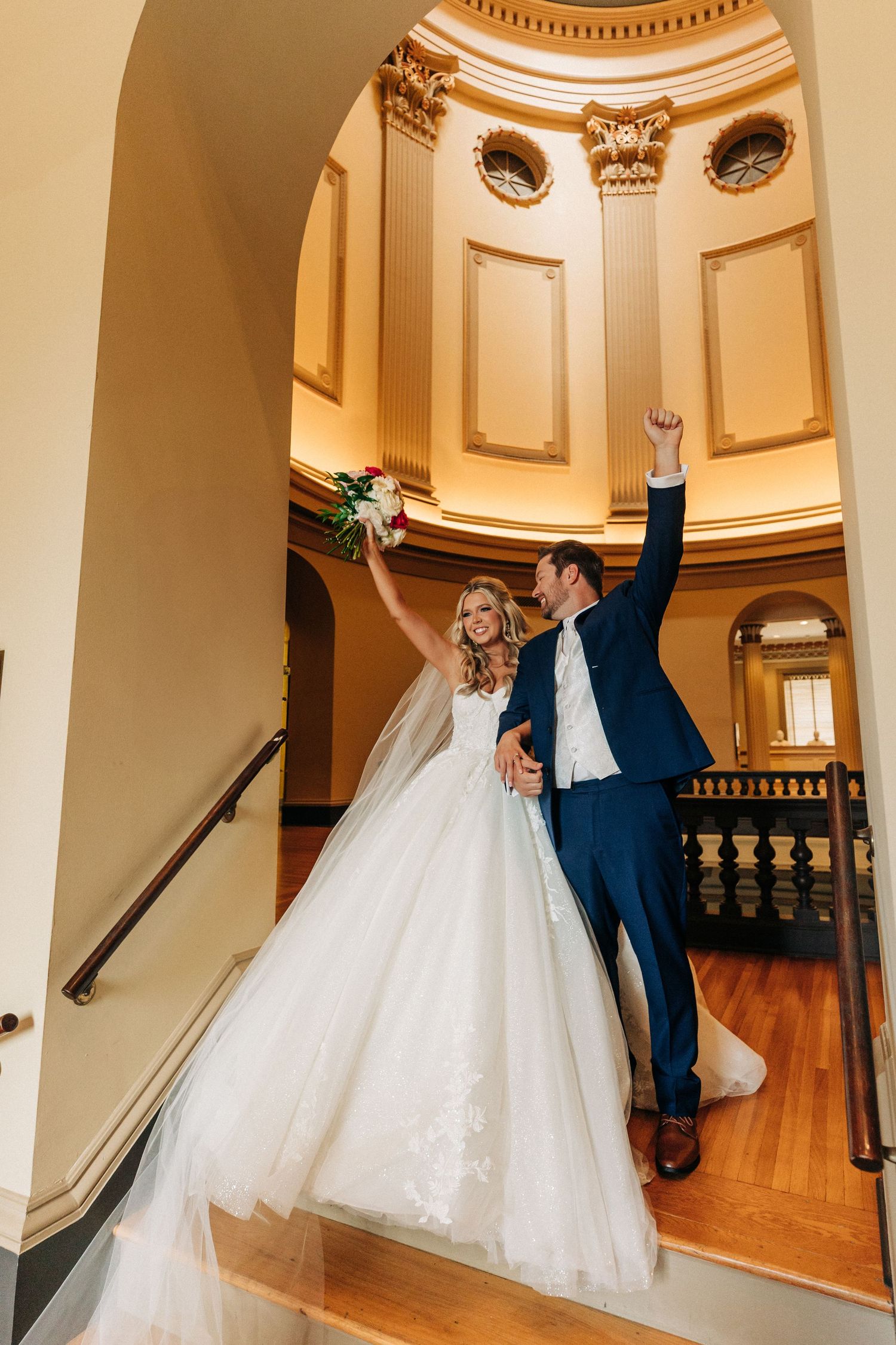 Joyful bride and groom celebrate in an elegant domed hallway with ornate architectural details and warm lighting.