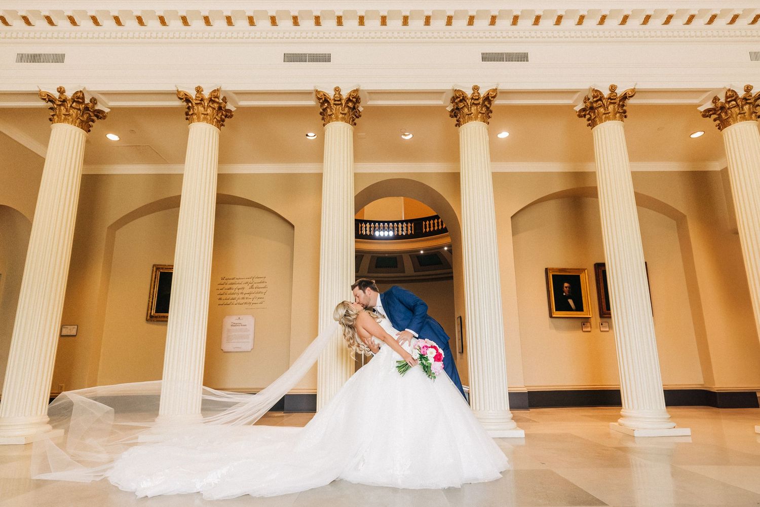 A couple shares a romantic moment in an elegant white-columned hallway with a sweeping wedding dress train.