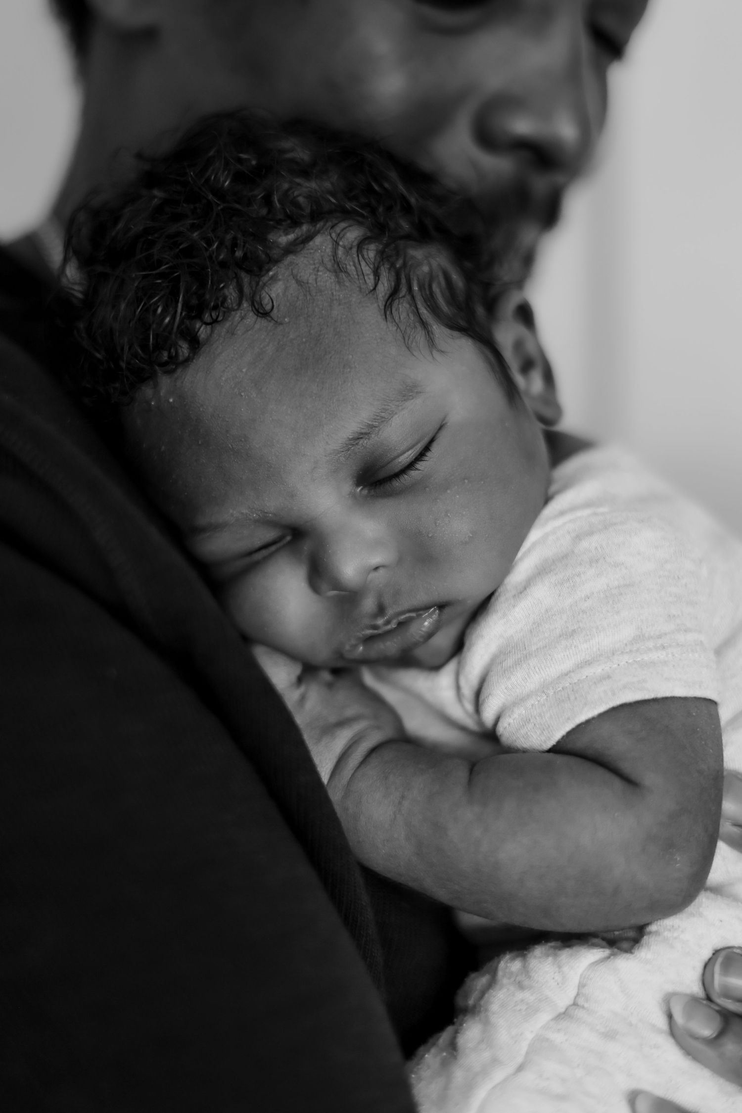 A peaceful black and white portrait of a sleeping baby resting against an adult wearing dark clothing.