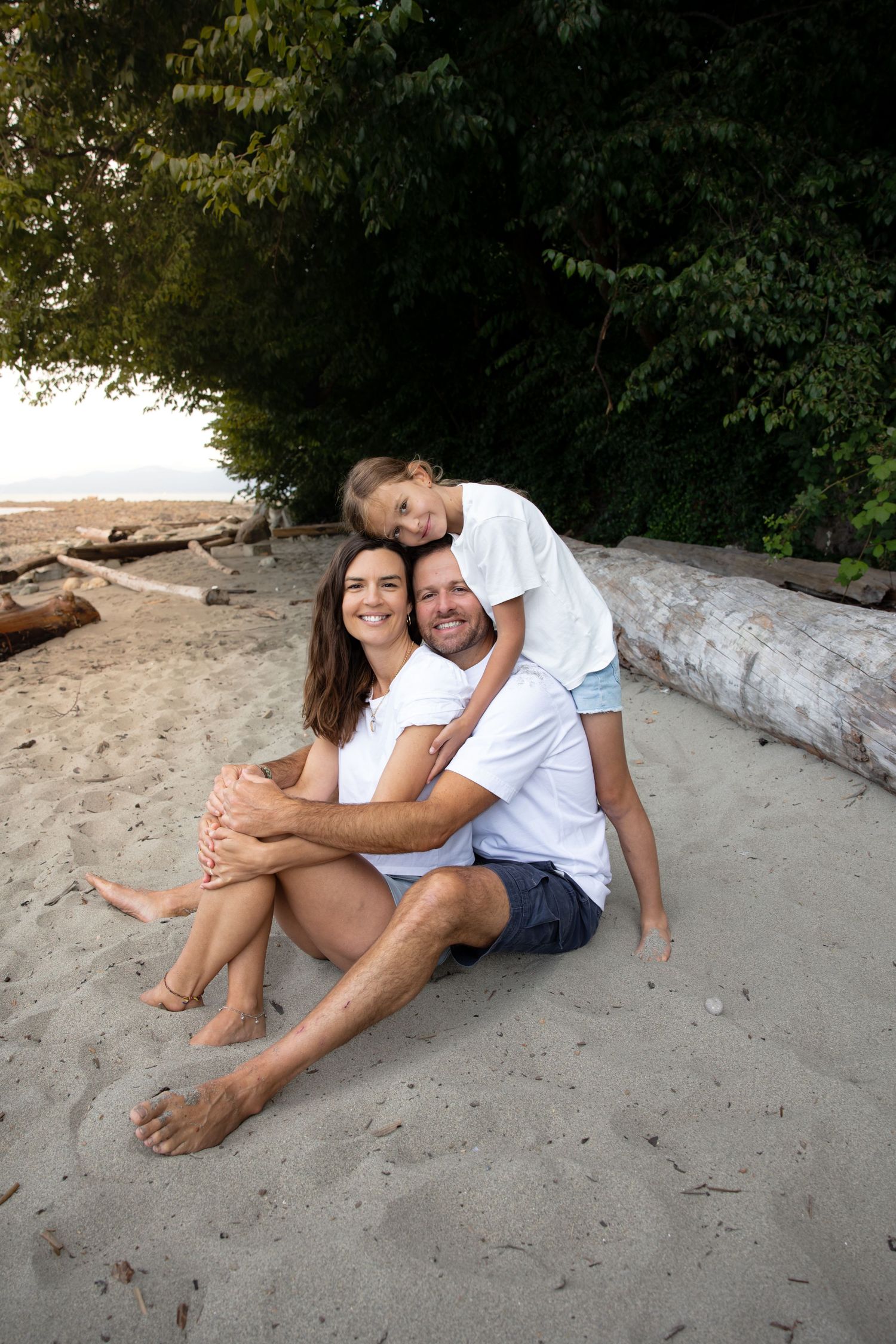 A couple in white and blue outfits relaxes together on a sandy beach near fallen driftwood logs.
