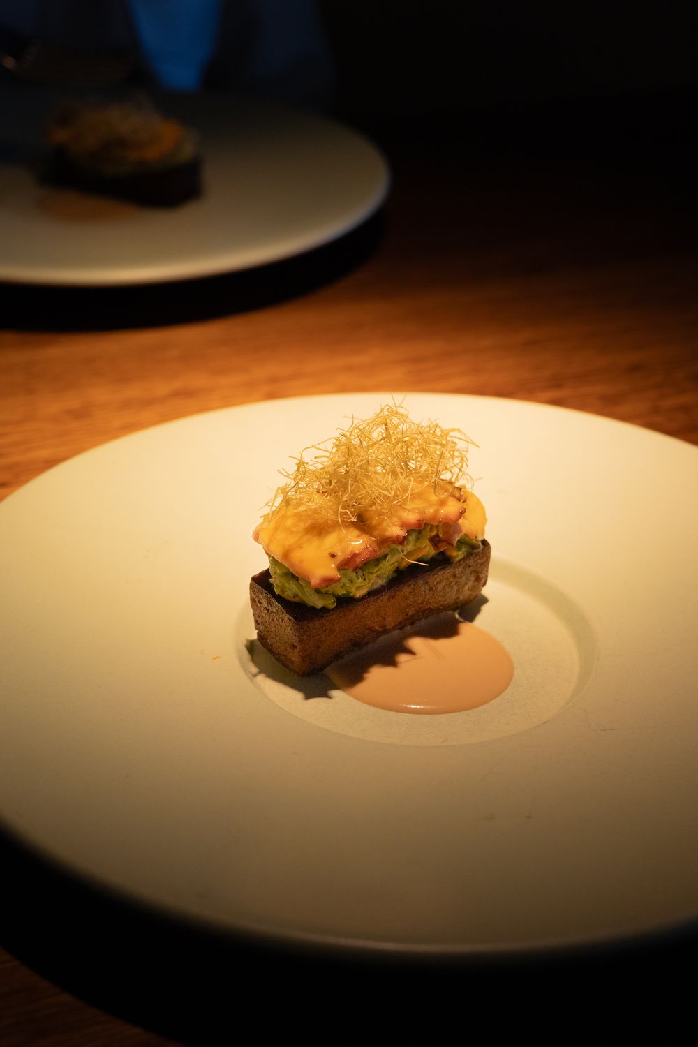 Elegant plated dishes with varied textures and ingredients served on white plates in dramatic lighting at upscale restaurant.