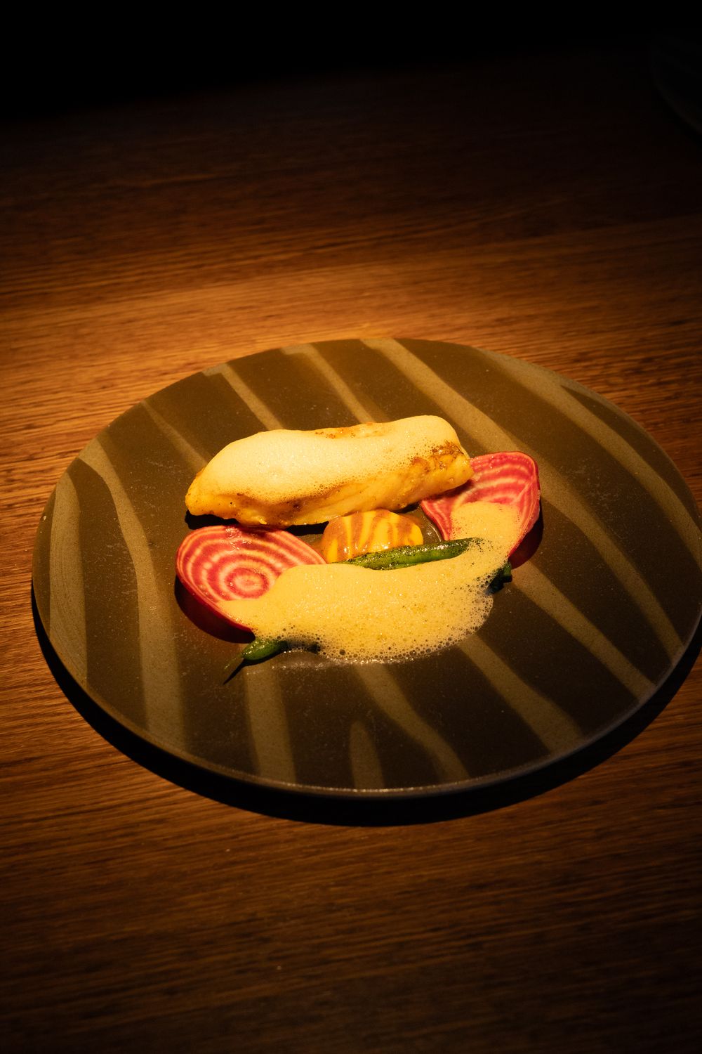 A sandwich with red beet slices served on a black striped plate under moody lighting.