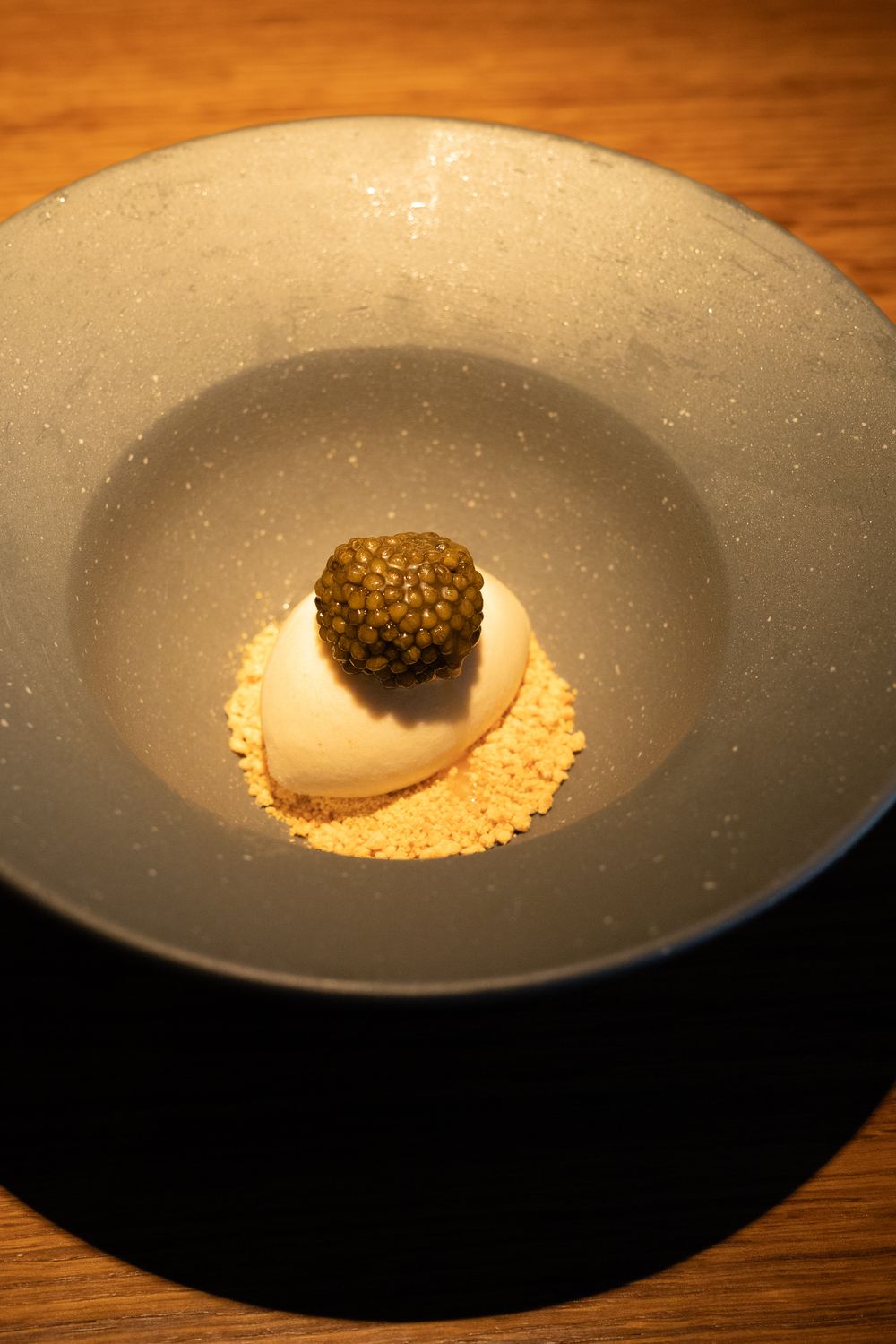 A minimalist plated dessert featuring a spherical truffle on powdered sugar in an elegant gray ceramic bowl.