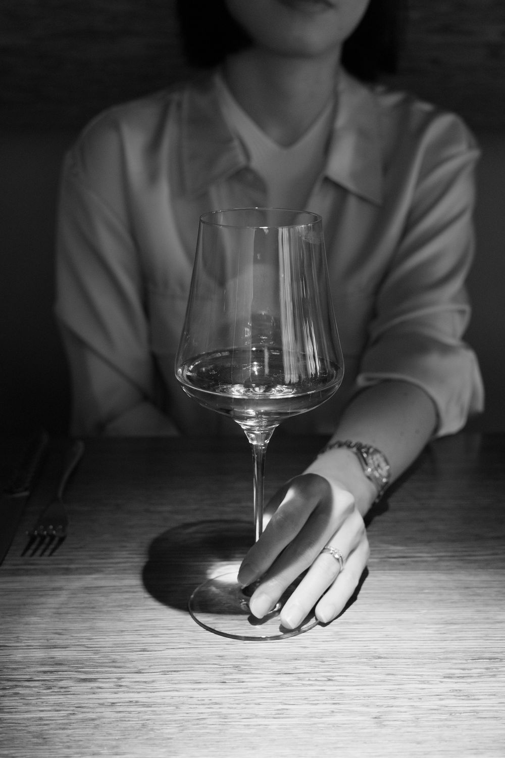 A series of dramatic black and white photos showing hands resting on a table next to wine glasses.