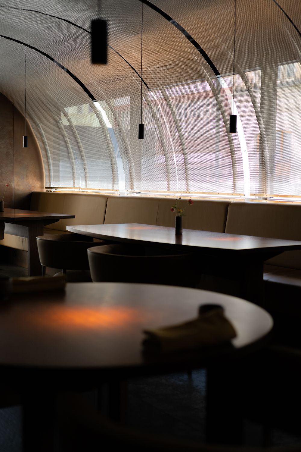 Curved booth seating in a dimly lit restaurant interior with modern pendant lights and a minimalist design aesthetic.