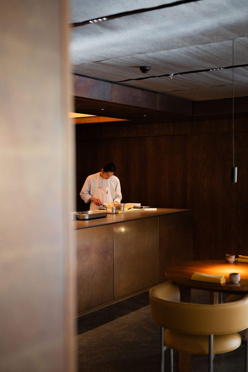 Modern restaurant interior with dark wood paneling and ambient lighting creates a sleek, minimalist dining atmosphere.