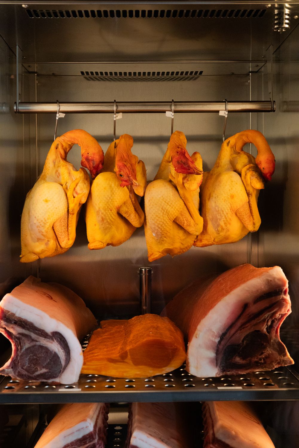 Raw turkey and ham portions displayed in a commercial food service refrigerator with metal shelving.