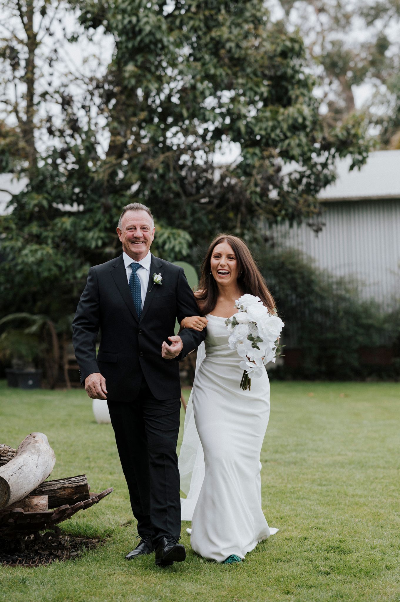 Wedding couple shares joyful moments on grassy lawn with natural backdrop.
