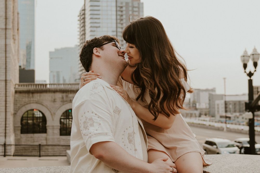 A romantic couple embraces on an urban rooftop with vintage lamp posts and city buildings in the background.
