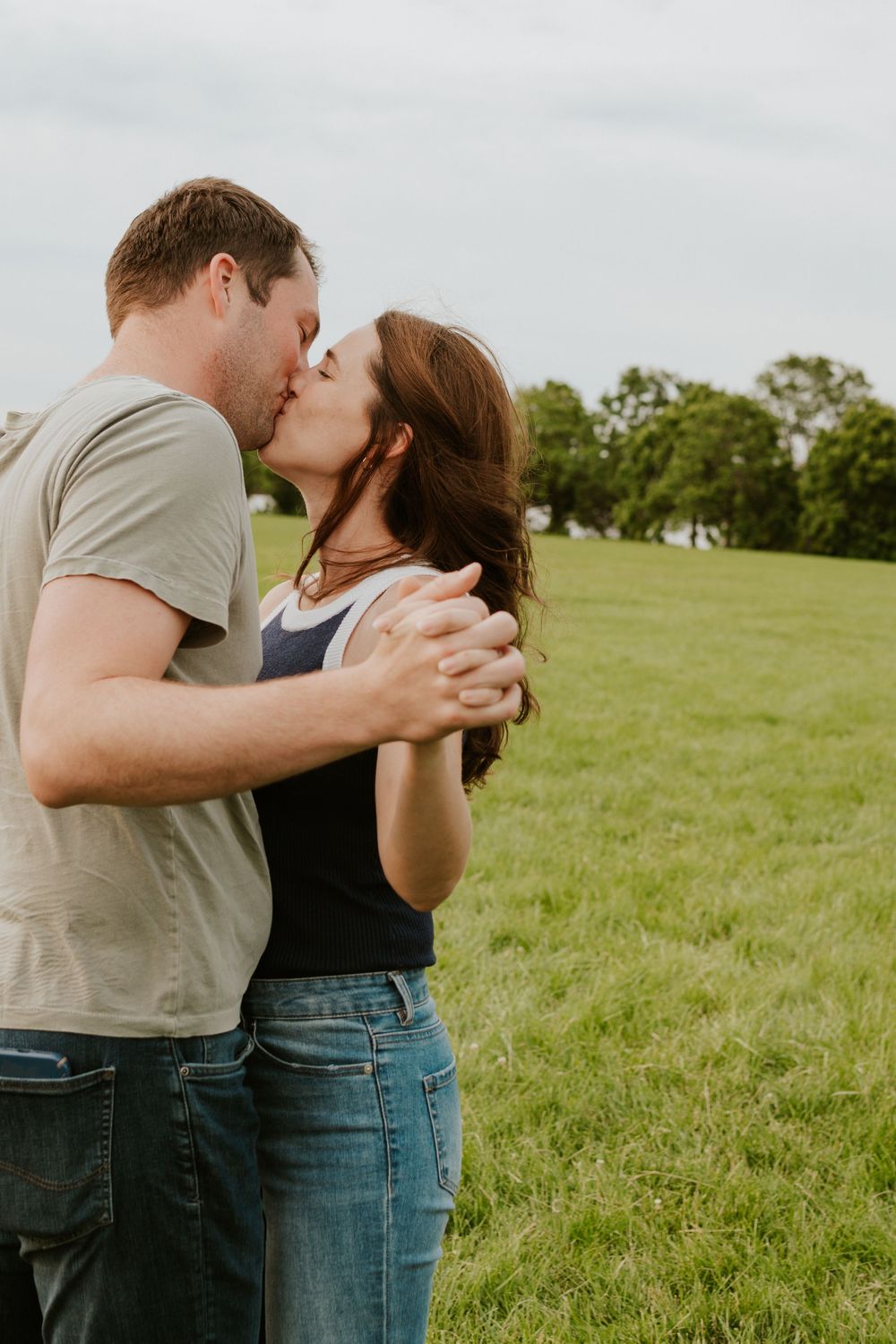 A romantic couple sharing a tender kiss in a green meadow on a sunny day.