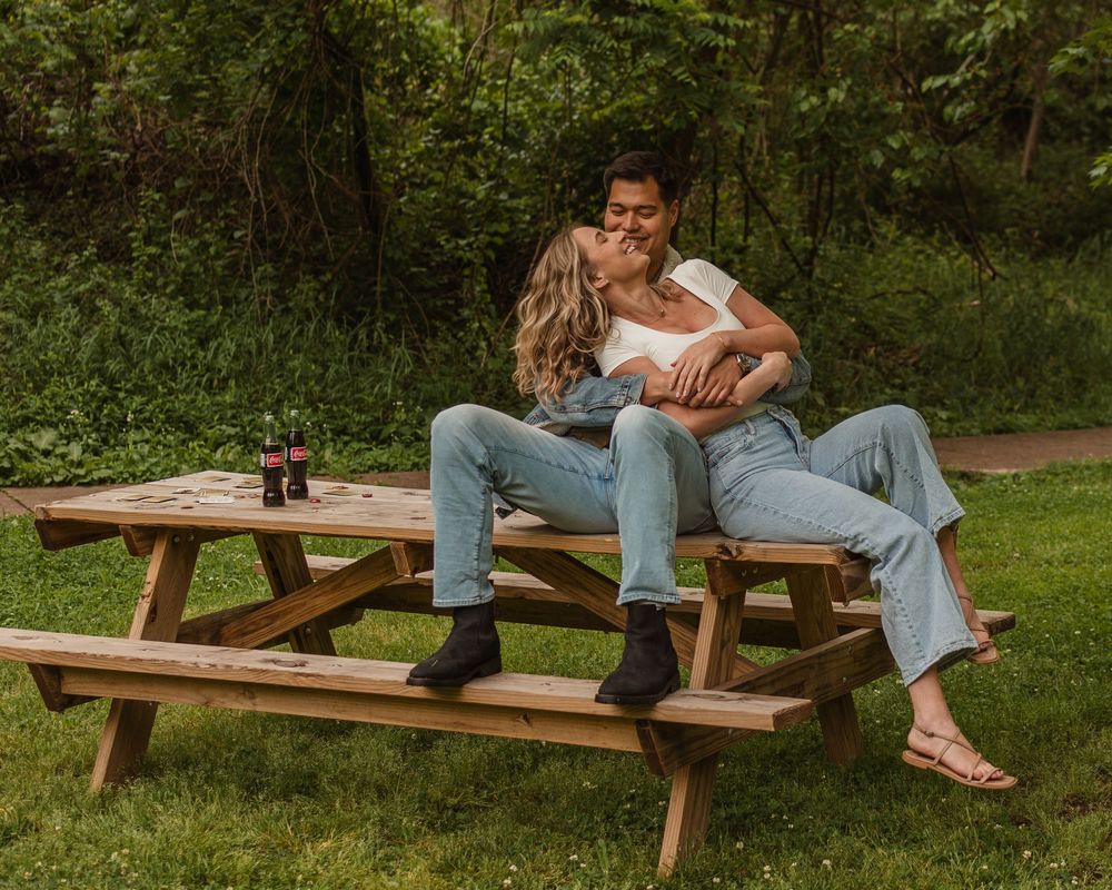 Group enjoying drinks and conversation while relaxing at a rustic picnic table in a green outdoor setting.
