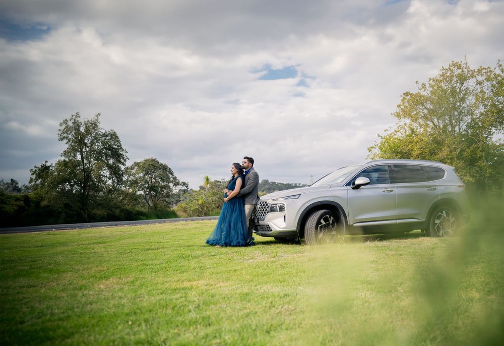 A silver SUV parked on a grassy hill under cloudy skies with figures and trees in the background.