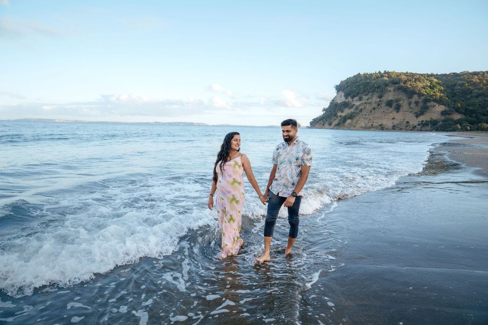 Couple walking along black sandy beach near cliffs with waves crashing against the shore during sunset.