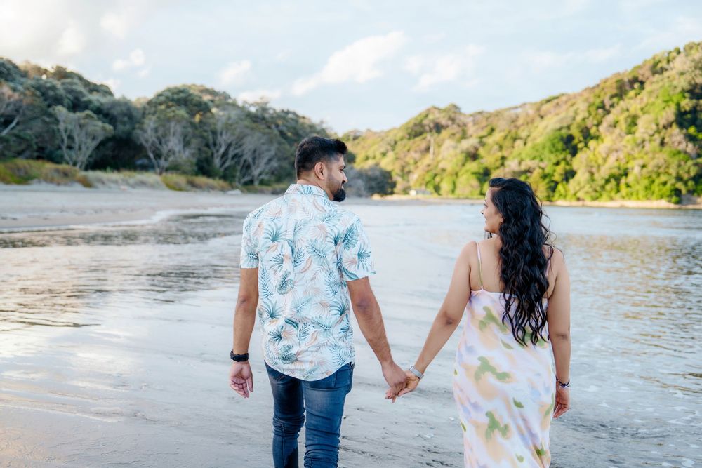 Couple holding hands while walking along a scenic beach with cliffs and ocean waves in the background.