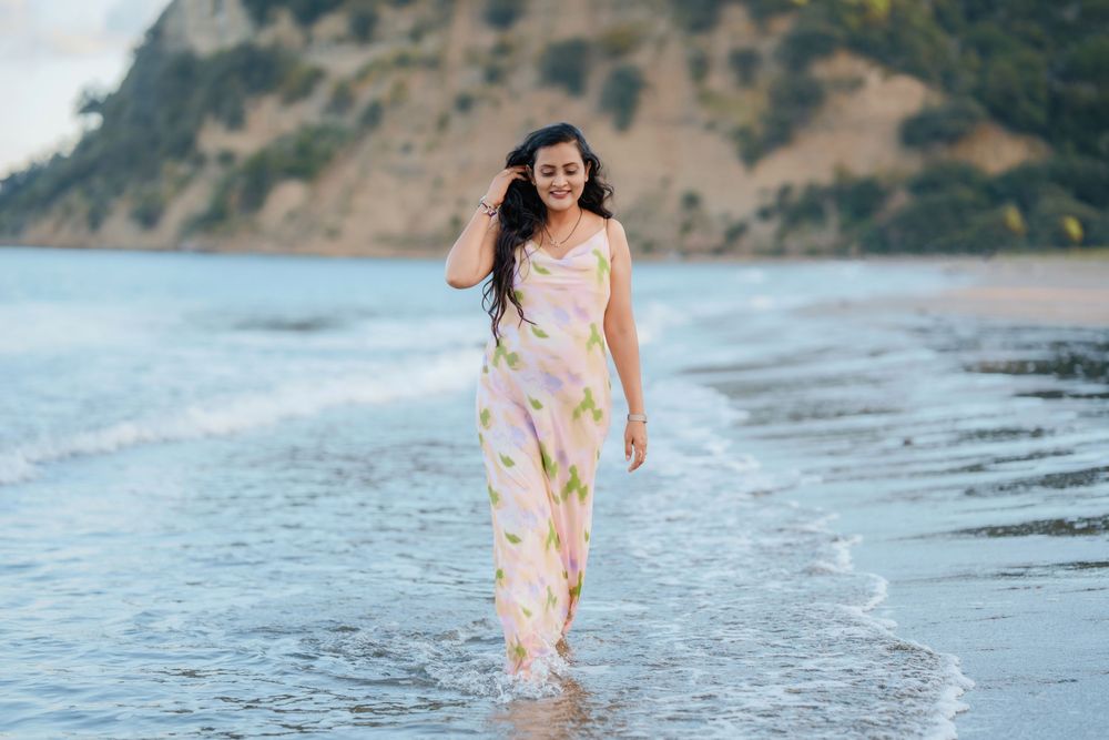 Someone in a floral maxi dress walks along the shoreline at a scenic beach with cliffs in the background.