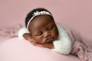 A peaceful sleeping baby wearing a delicate tiara lies on soft pink bedding with a white wrap. south sudanese baby, girl, ipswich, best phot