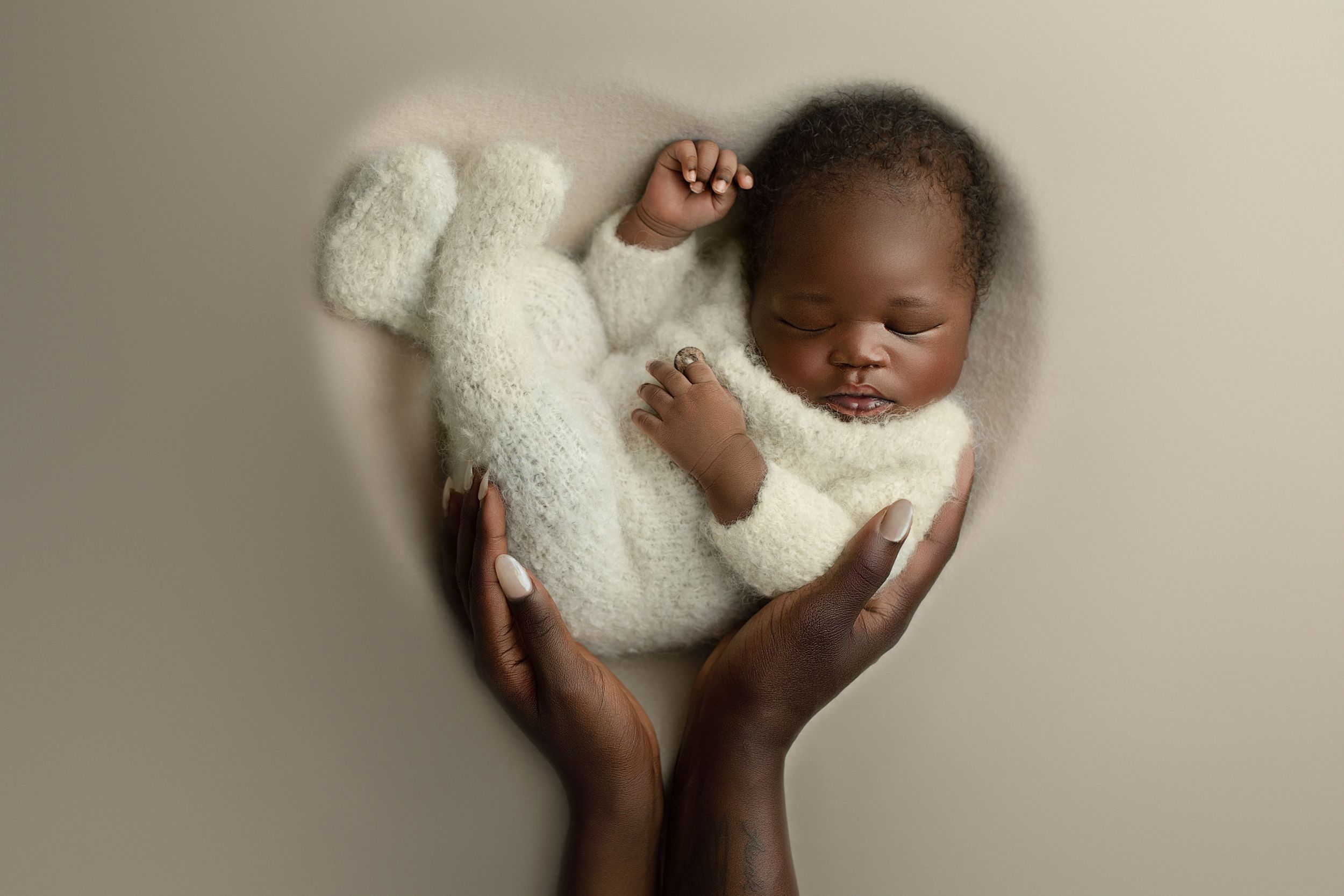 Newborn photography Brisbane and Ipswich – baby boy in soft white knit outfit cradled in parent’s hands at Springfield Lakes studio.