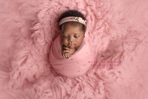 Newborn wrapped in pink fabric surrounded by soft pink textured material in studio portrait.