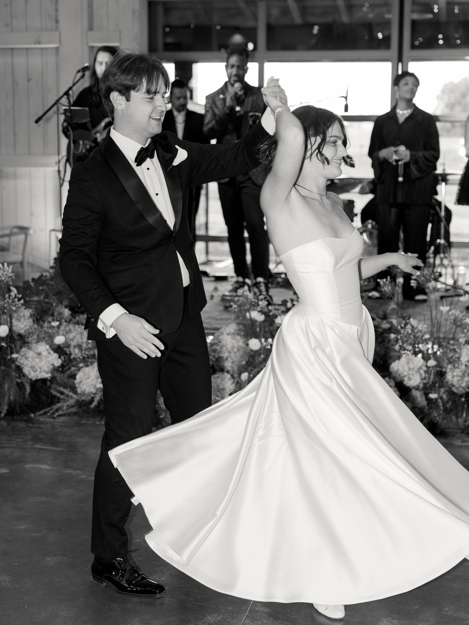 A couple in formal wedding attire dances together at their reception with a band performing in the background.