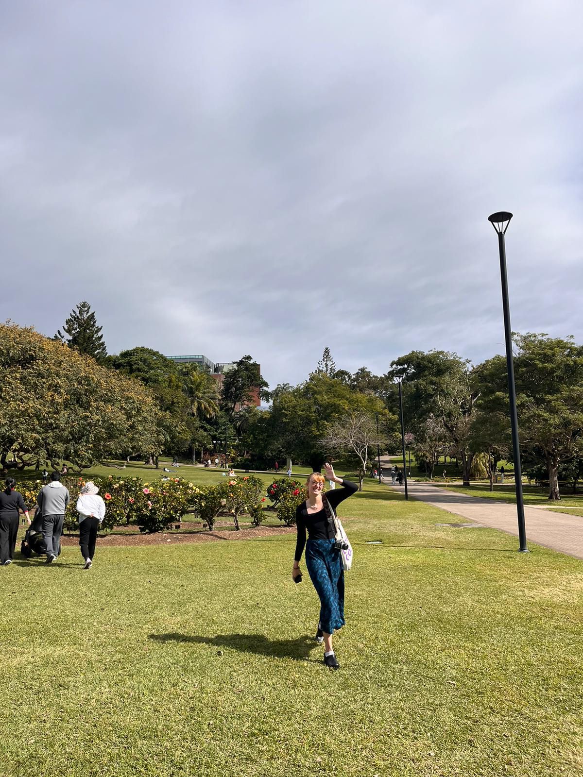 People playing frisbee together on a green grassy field in a park under cloudy skies.