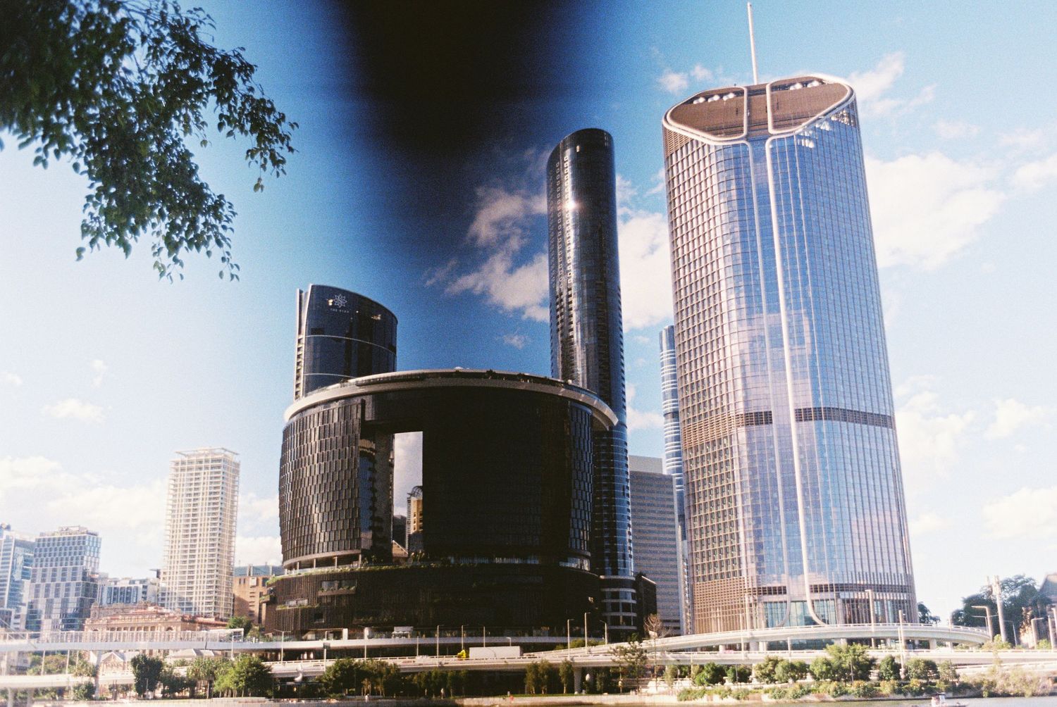 Modern city skyline featuring cylindrical industrial buildings and glass skyscrapers against blue sky.