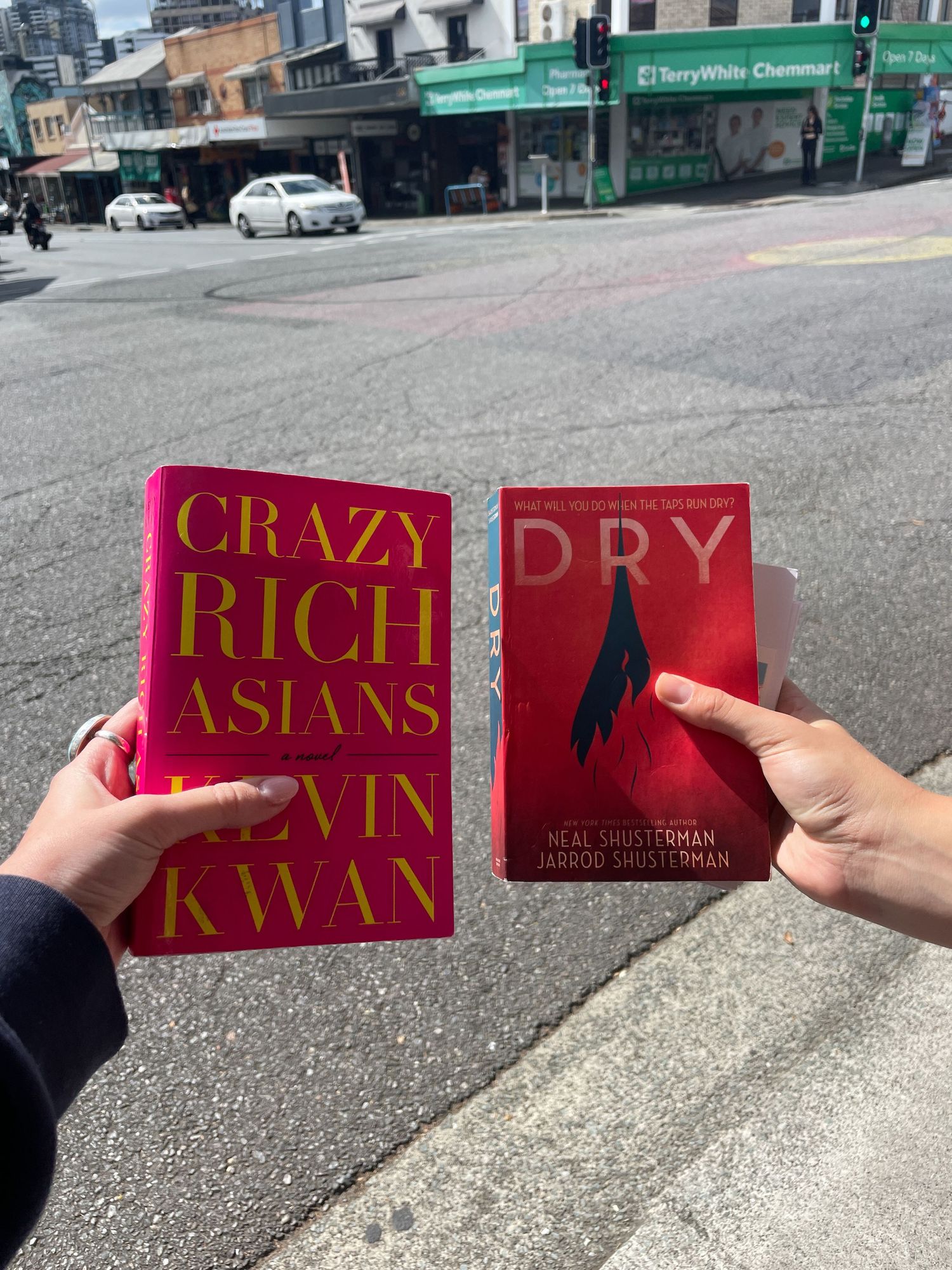 Red hardcover books from Kevin Kwan's Crazy Rich Asians series displayed against urban street background.