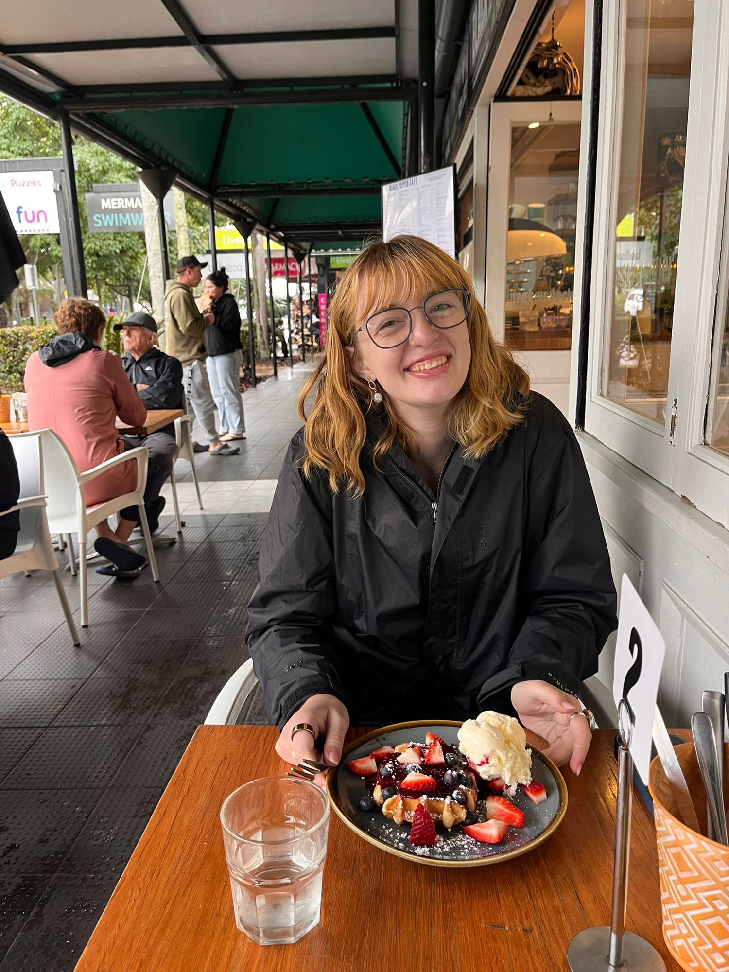 Someone seated at an outdoor cafe table with a colorful fruit and berry dish.