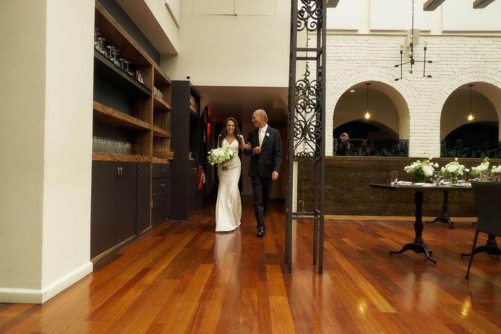 A couple walks down a hallway with hardwood floors in a venue with white walls and decorative black ironwork at the Milling Room