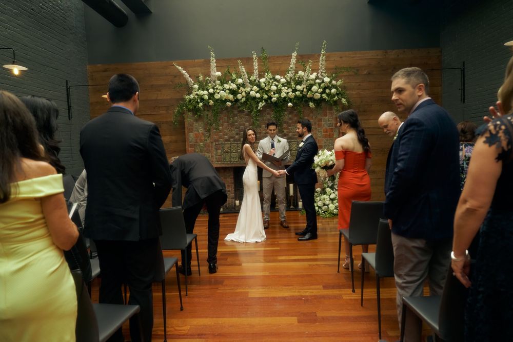 A wedding ceremony takes place in an intimate indoor venue with a floral arch and wooden decor at the Milling Room