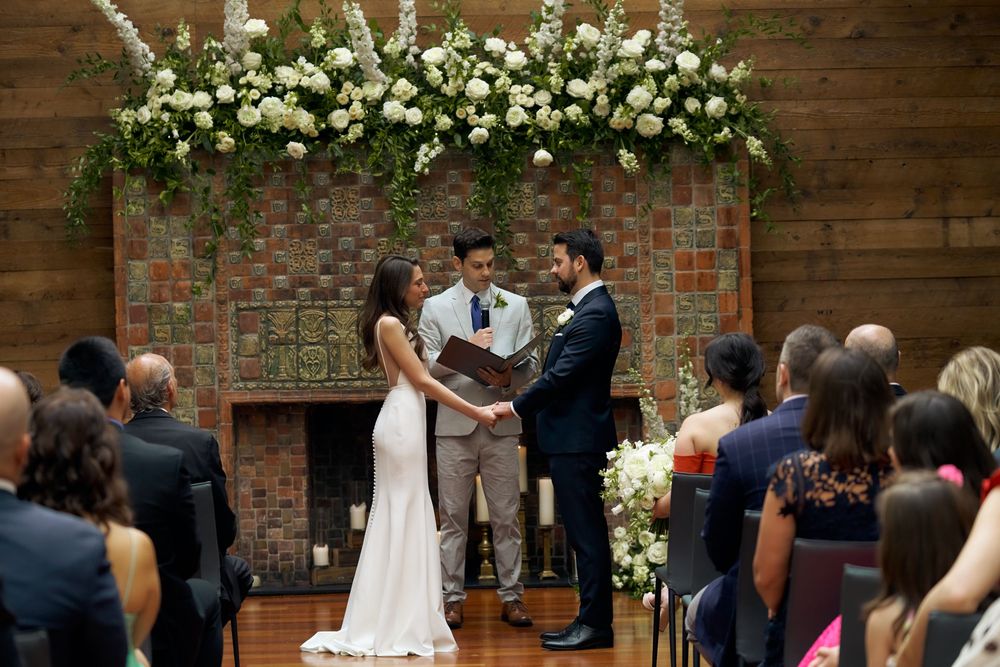 Wedding ceremony in a rustic brickwalled venue with white floral decorations and guests gathered to witness the occasion at the Milling Room
